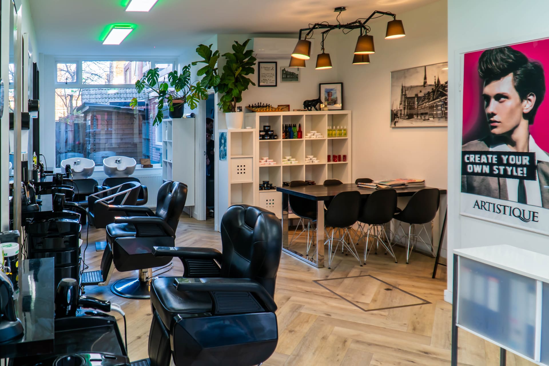 Het interieur van Kapsalon Assendorp met zwarte kappersstoelen, wasbakken en een leestafel.
