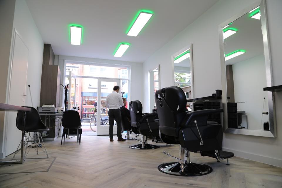 Zicht door de salon naar de voordeur, met kappersstoelen en spiegels aan weerszijden.