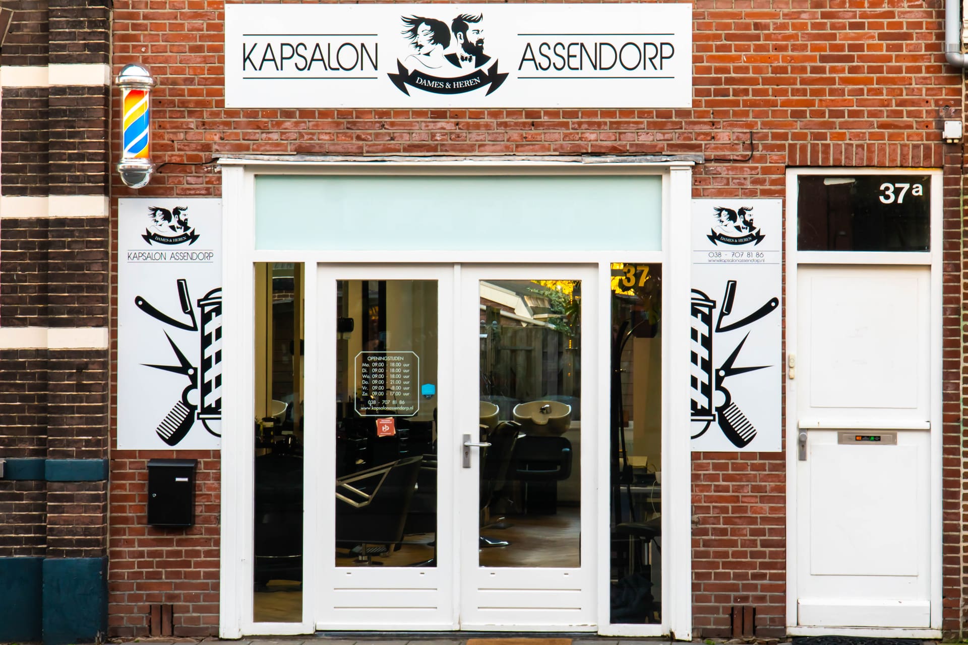 De gevel van Kapsalon Assendorp met het witte uithangbord en de barberpaal aan de Assendorperstraat.